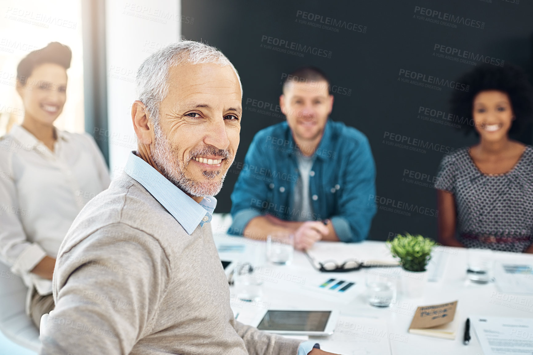 Buy stock photo Portrait of a mature businessman sitting in a meeting with his colleagues in the background
