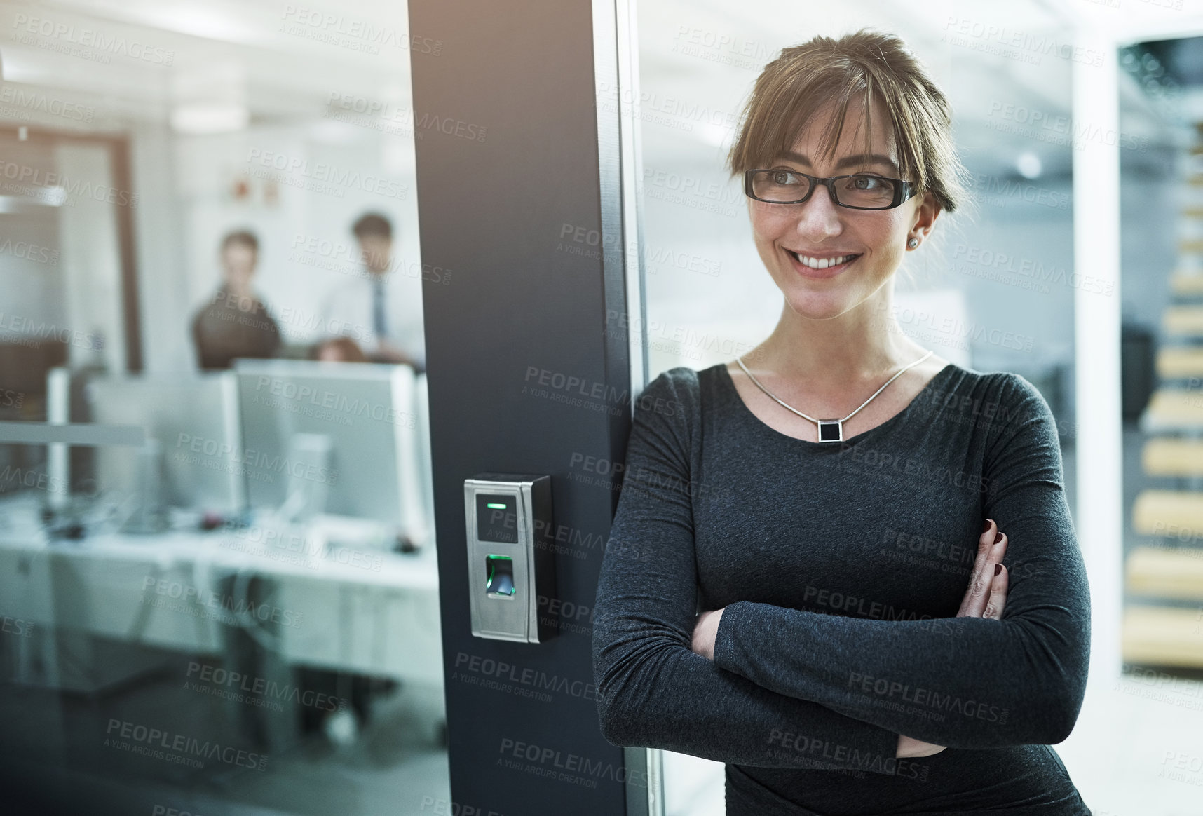 Buy stock photo Shot of a young businesswoman standing with her arms crossed in an office doorway