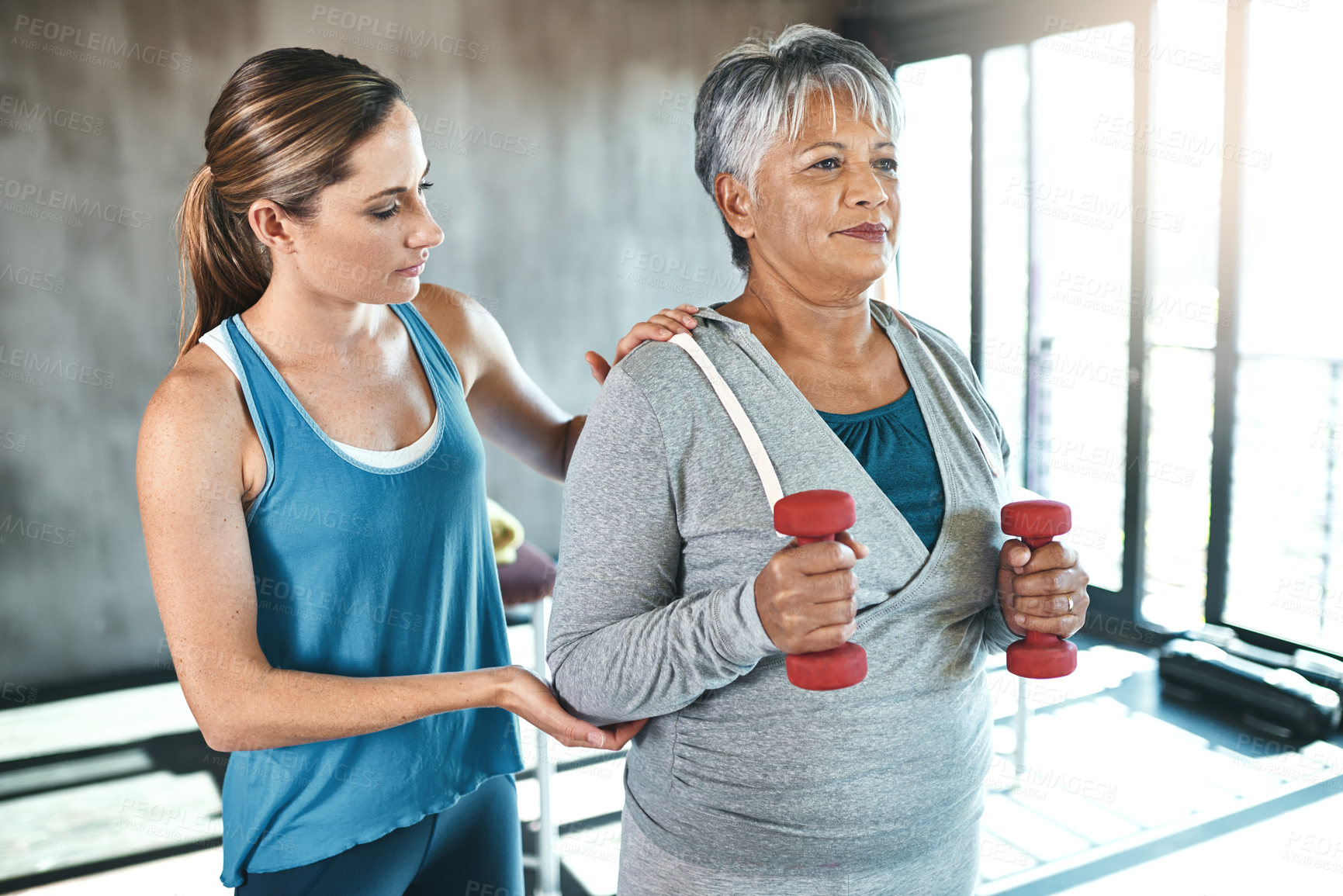 Buy stock photo Senior woman, dumbbells and help with coach in gym for physio, stretching arms and rehabilitation exercise. Old female patient, instructor support and workout for arthritis with balance and weights