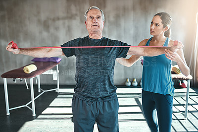 Buy stock photo Shot of a senior man using resistance bands with the help of a physical therapist