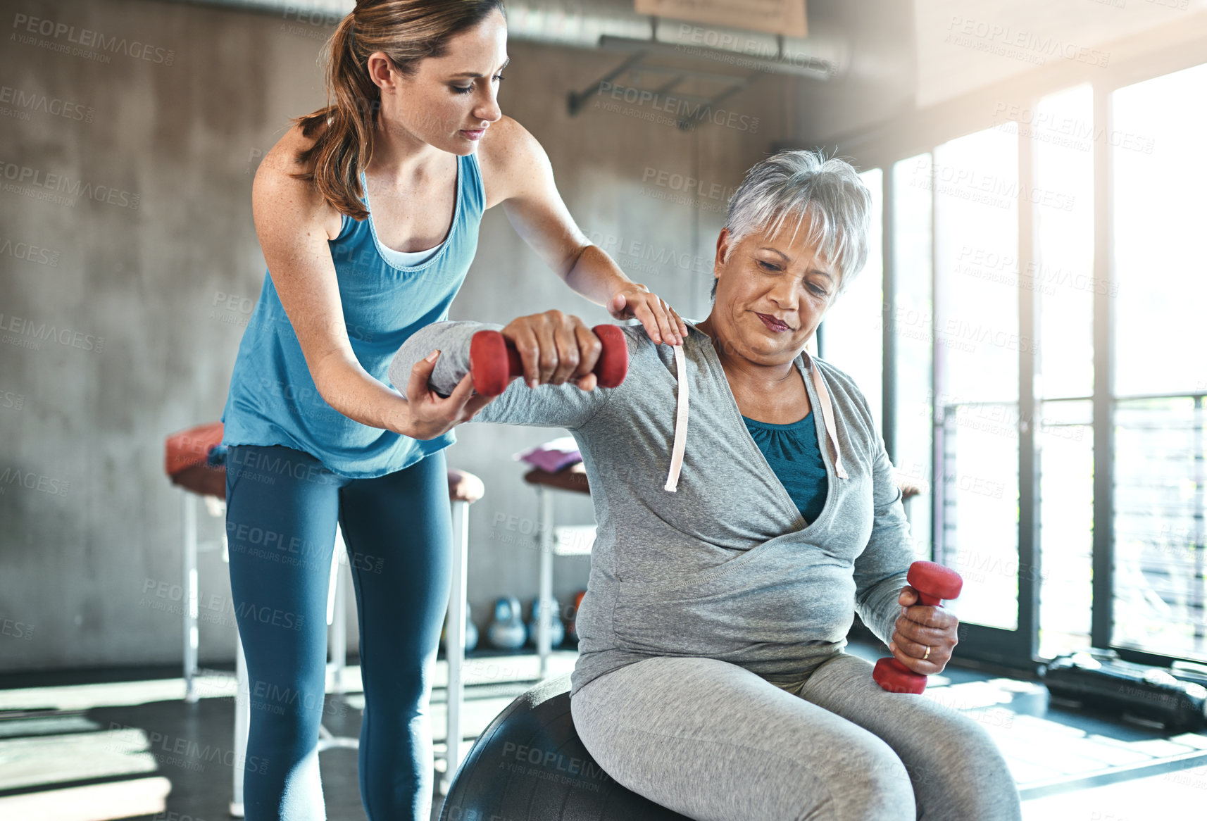 Buy stock photo Senior woman, weights and helping with coach in gym for physio, arm exercise and rehabilitation on ball. Old female patient, instructor and workout equipment for arthritis with balance and dumbbells