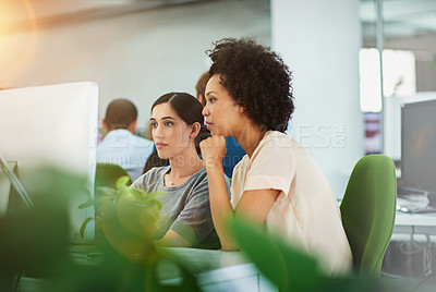 Buy stock photo Shot of two young designers talking together while working on a computer in a modern office