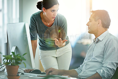 Buy stock photo Shot of two designers talking together while working on a computer in a modern office