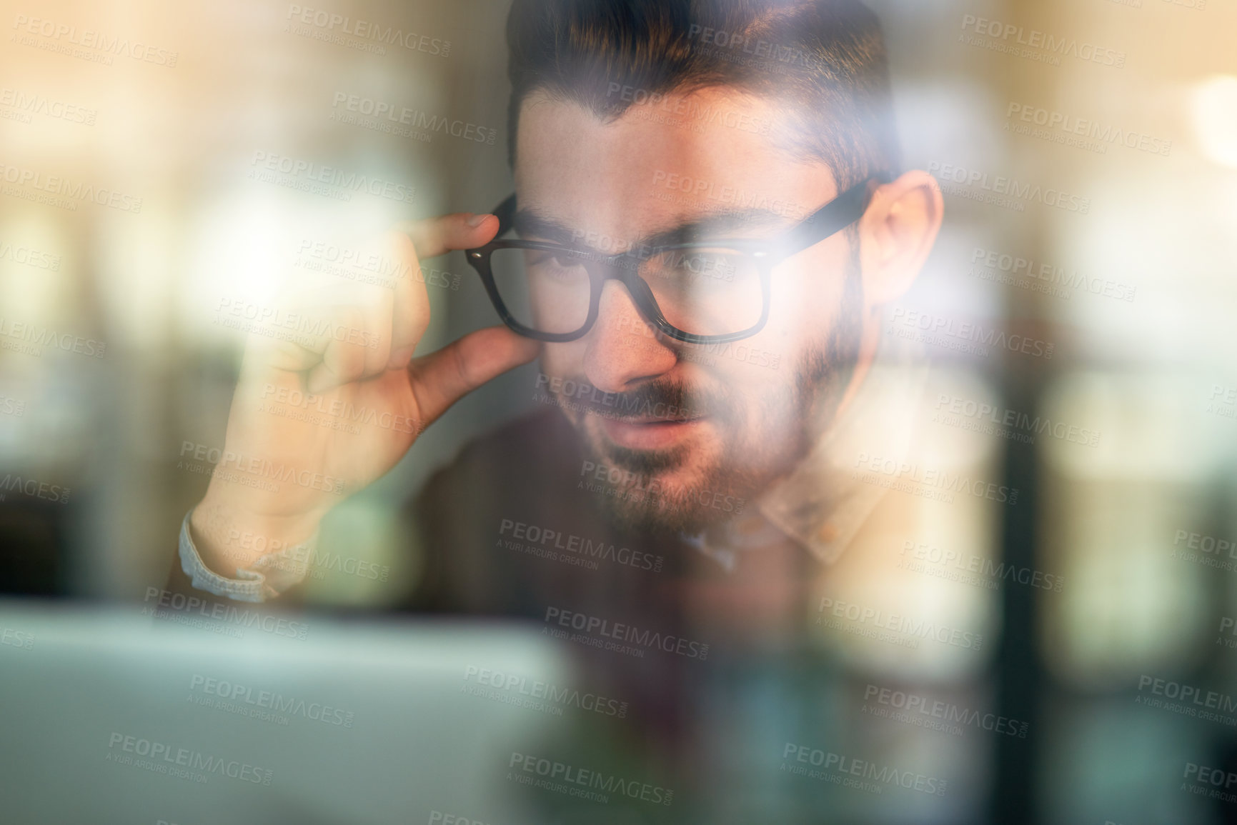 Buy stock photo Shot of a focused young programmer working on his computer behind a glass wall