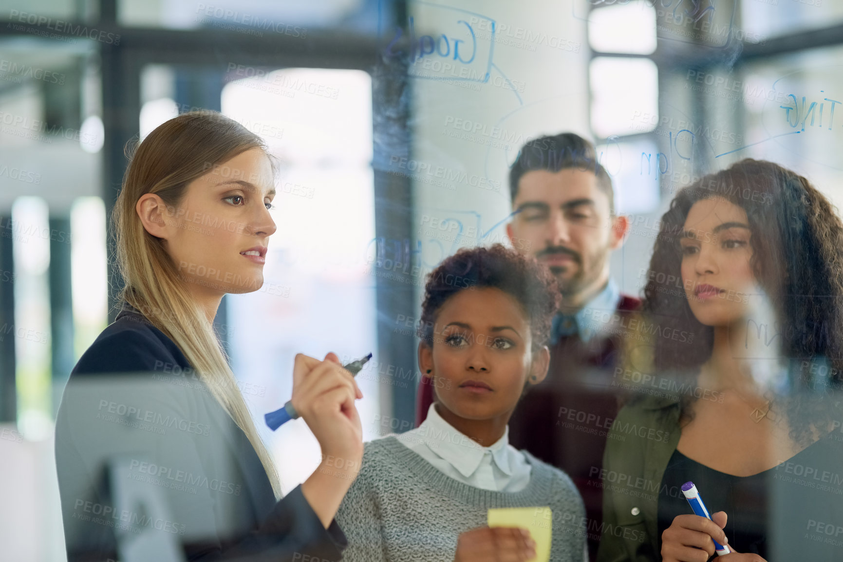 Buy stock photo Shot of a group of young entrepreneurs brainstorming with notes on a glass wall in an office