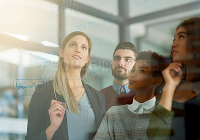 Buy stock photo Shot of a group of young entrepreneurs brainstorming with notes on a glass wall in an office