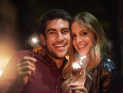 Buy stock photo Shot of a happy young couple celebrating with sparklers outside at night