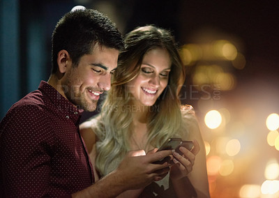 Buy stock photo Shot of a young couple using their smartphones together at night
