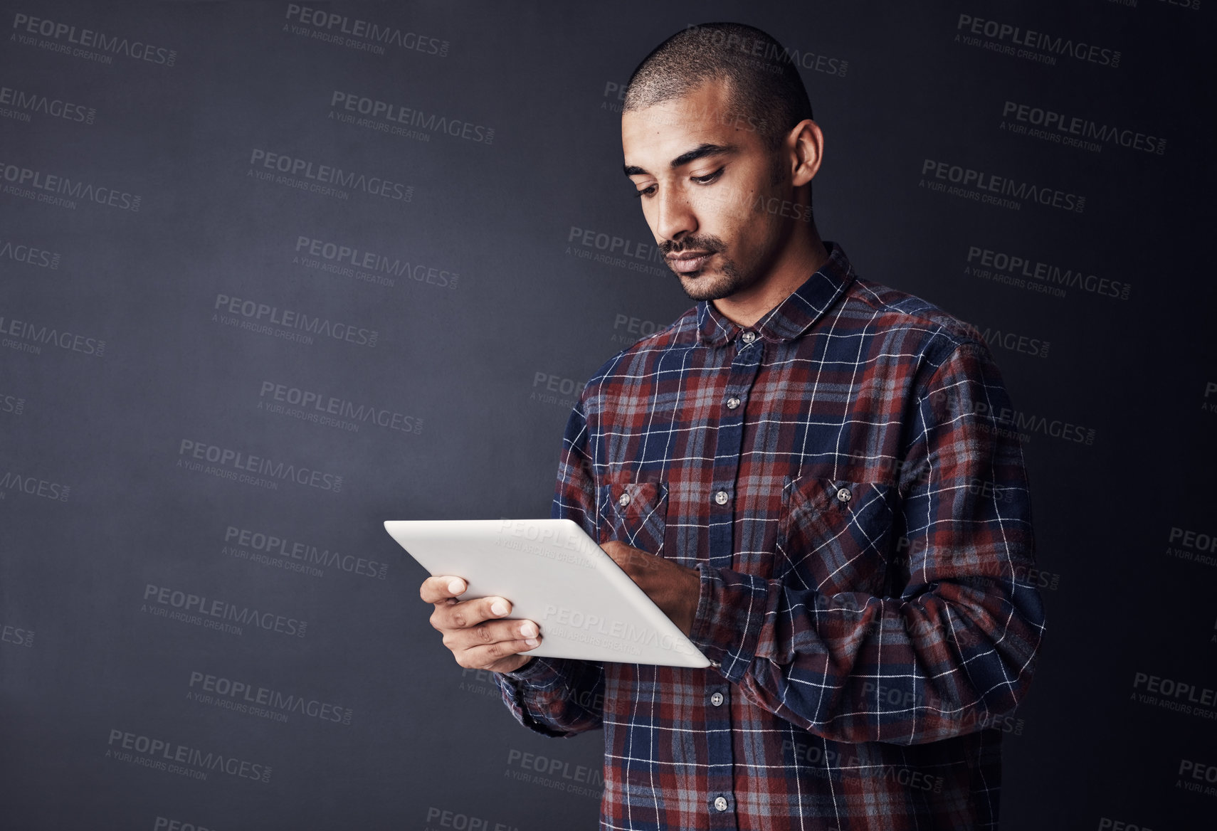 Buy stock photo Studio shot of a young man using a digital tablet against a dark background