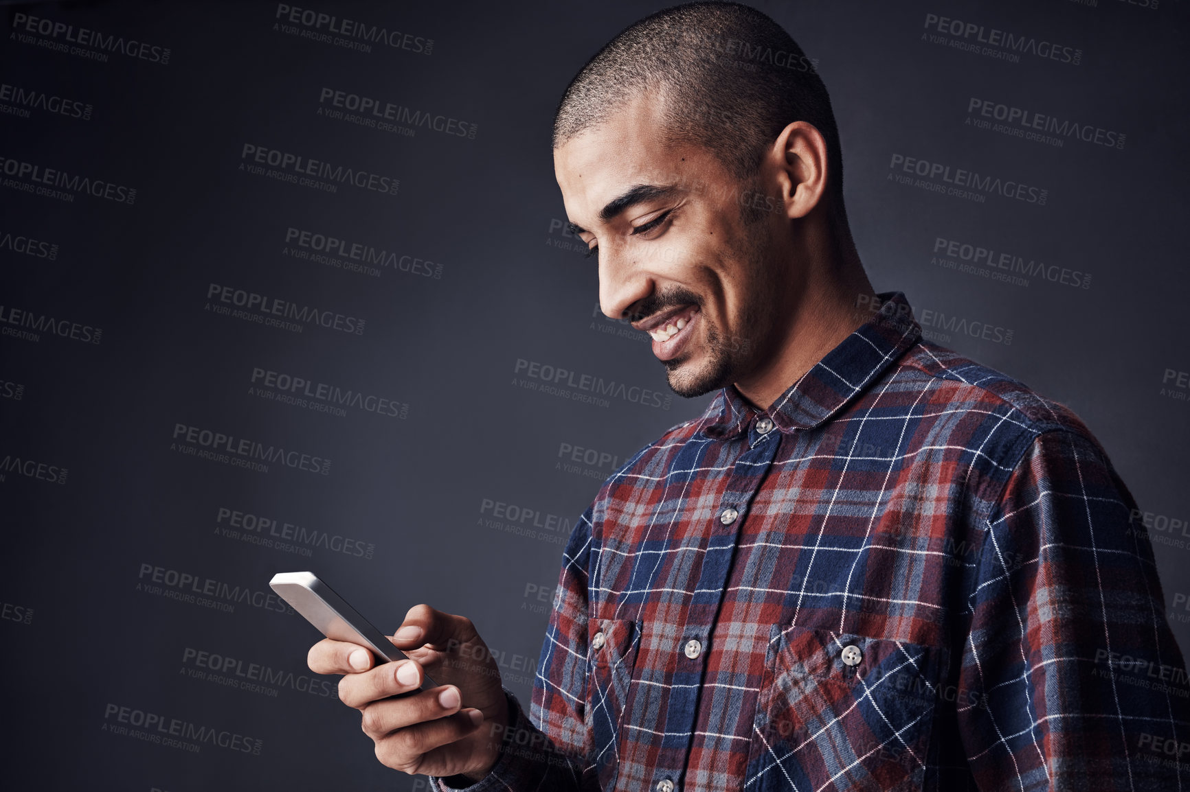 Buy stock photo Studio shot of a young man texting on a cellphone against a dark background