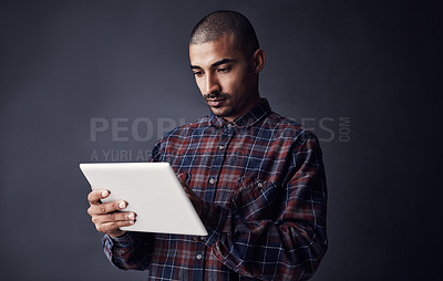Buy stock photo Studio shot of a young man using a digital tablet against a dark background