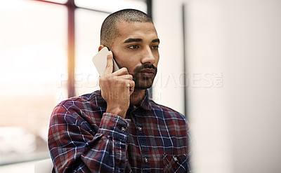 Buy stock photo Shot of a young entrepreneur talking on a cellphone while working on a computer in an office
