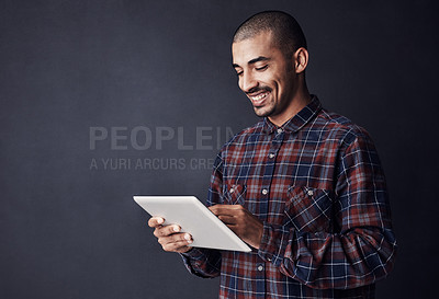 Buy stock photo Studio shot of a young man using a digital tablet against a dark background