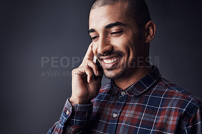Buy stock photo Studio shot of a young man talking on a cellphone against a dark background