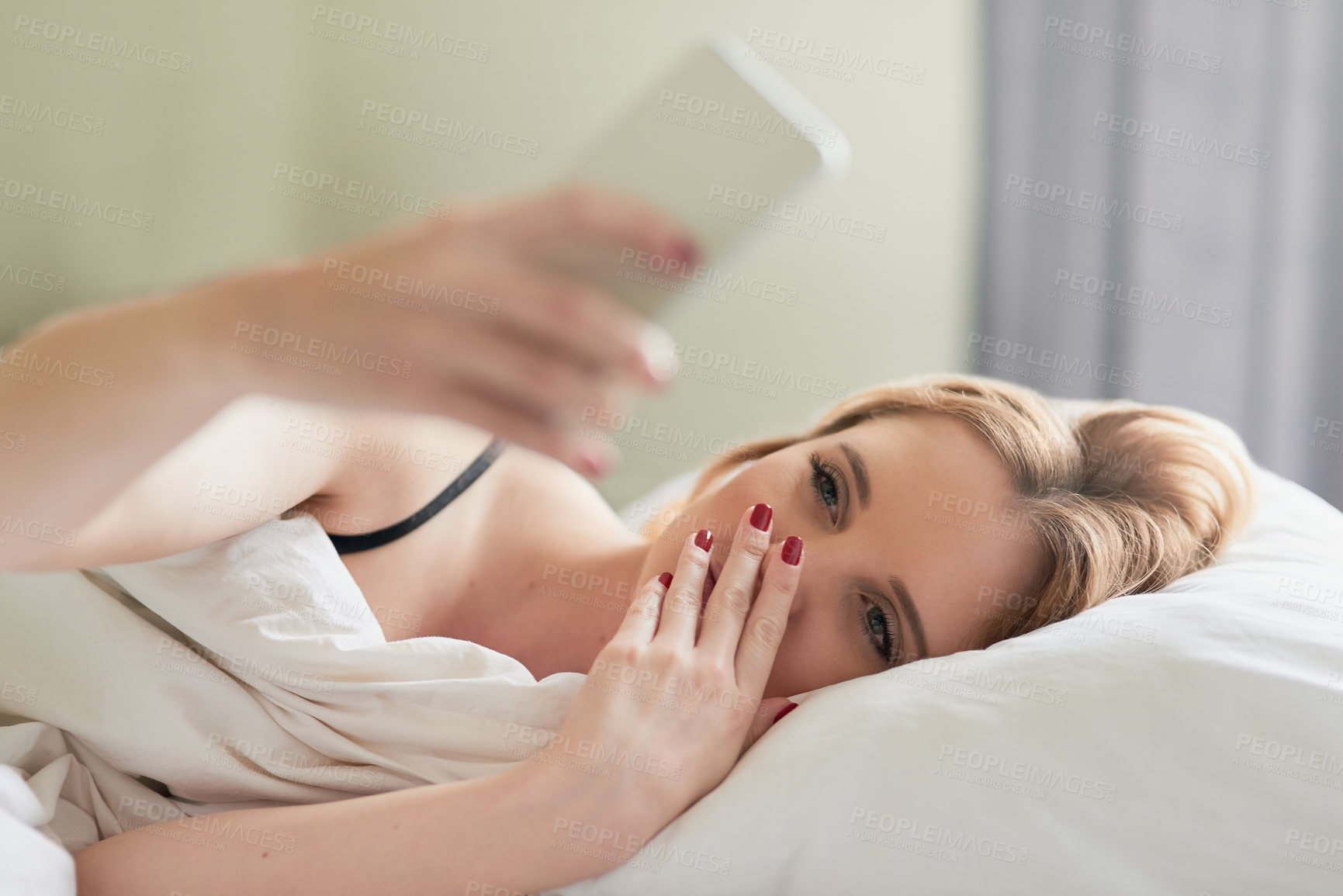 Buy stock photo Shot of an attractive young woman texting on her cellphone while lying in her bed at home