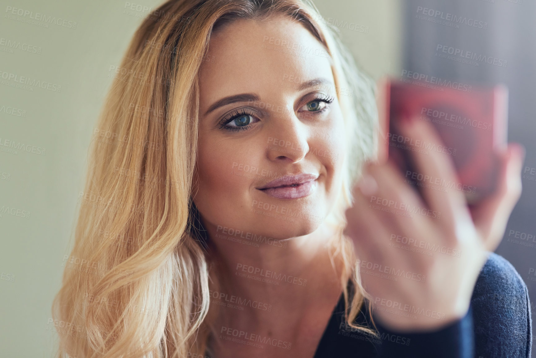 Buy stock photo Shot of an attractive young woman looking at her face in a compact mirror