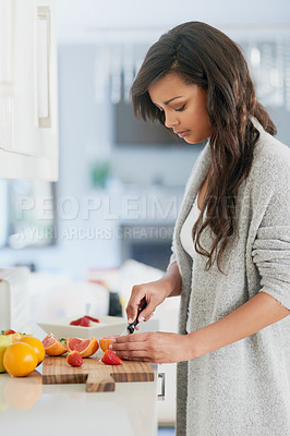 Buy stock photo Shot of young woman cutting fruit for breakfast in her kitchen at home