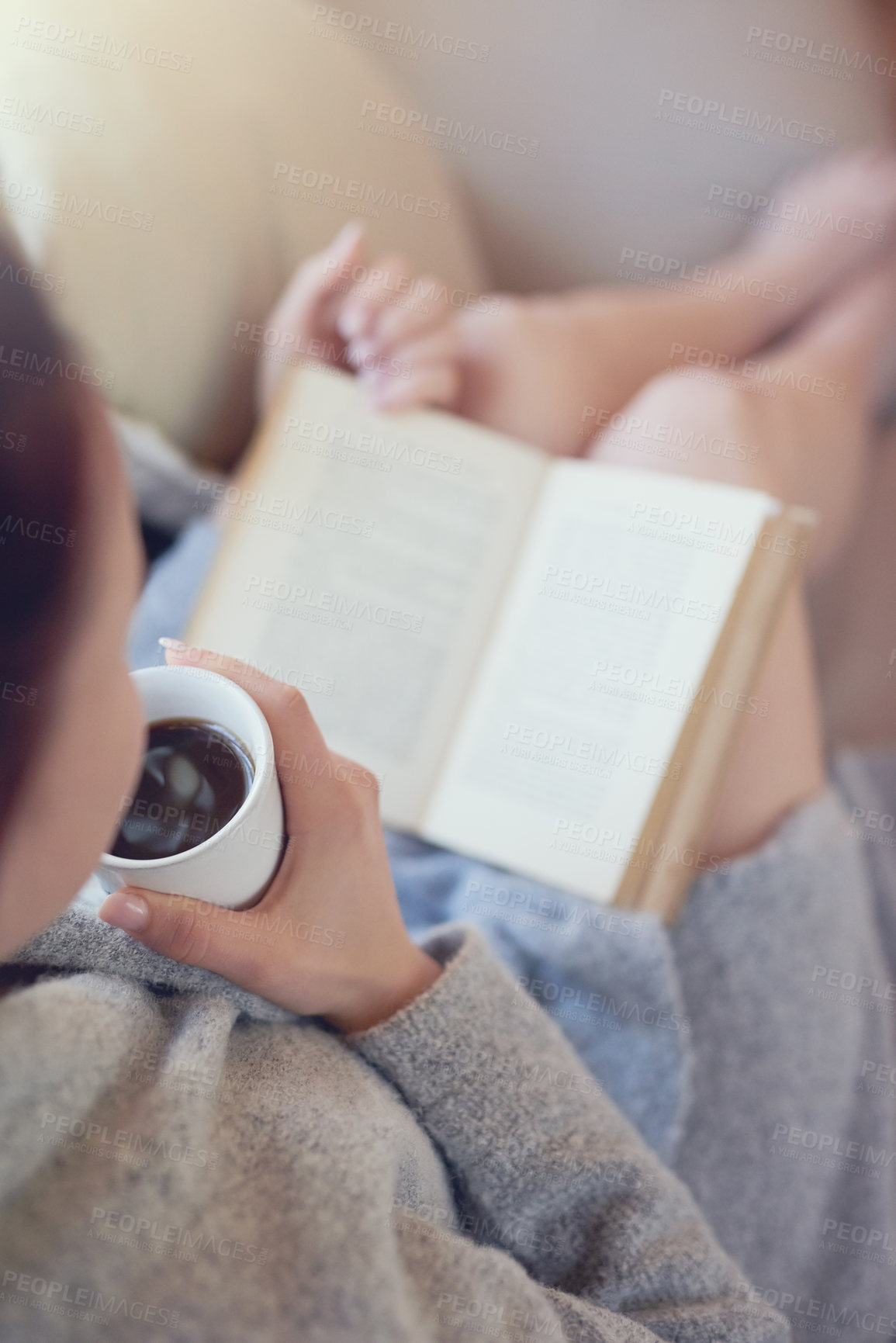 Buy stock photo Cropped shot of a woman relaxing with a book and cup of coffee at home