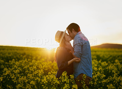 Buy stock photo Shot of an affectionate young couple sharing a kiss at sunset
