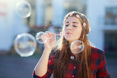 Buy stock photo Shot of an attractive young woman blowing bubbles outside