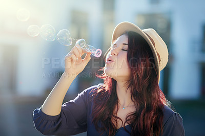 Buy stock photo Shot of an attractive young woman blowing bubbles outside