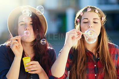 Buy stock photo Shot of two young friends blowing bubbles together outside