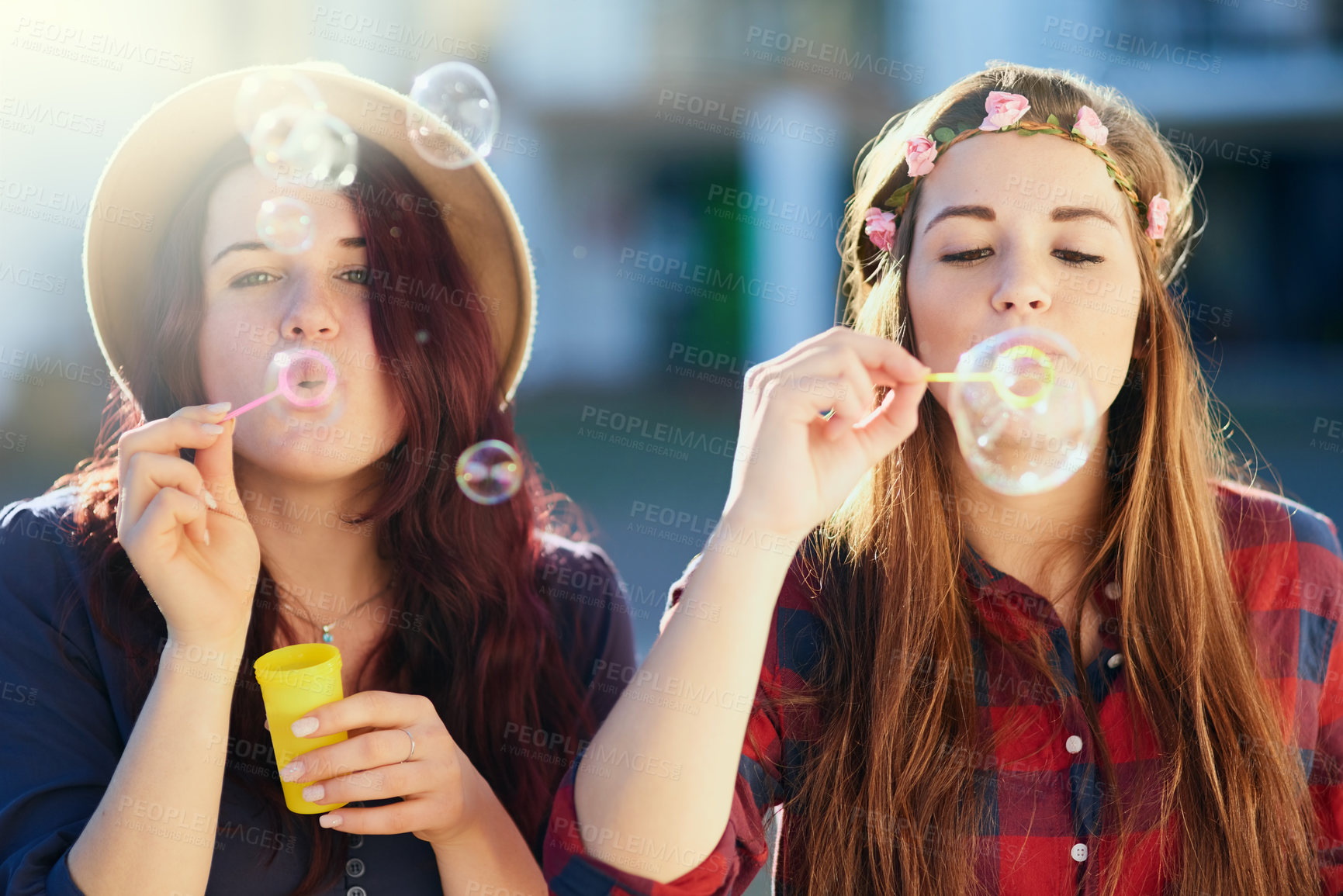 Buy stock photo Shot of two young friends blowing bubbles together outside