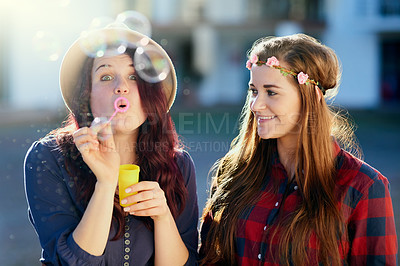 Buy stock photo Shot of two young friends blowing bubbles outside