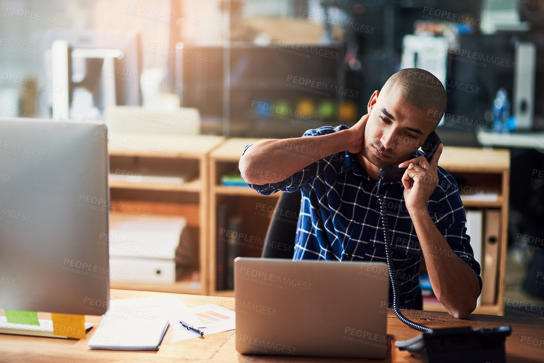 Buy stock photo Cropped shot of a young designer looking stressed out while talking on a phone in an office