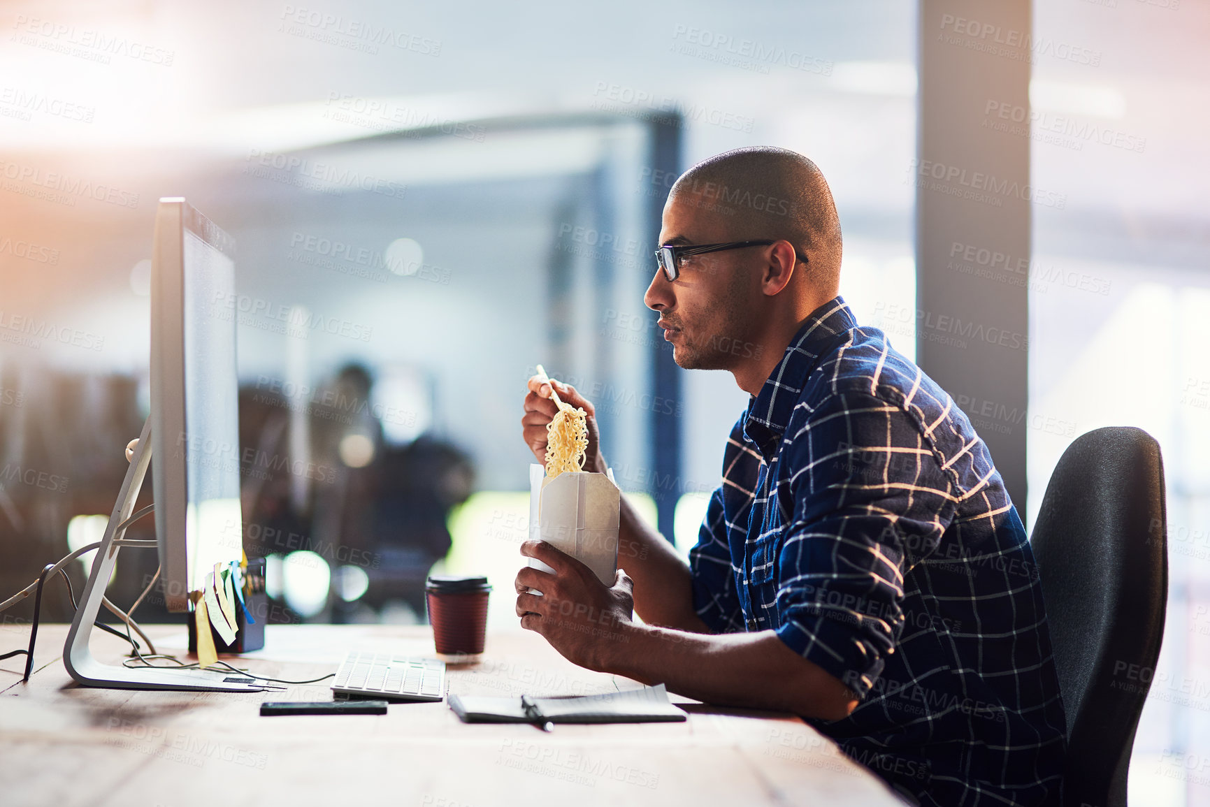 Buy stock photo Portrait of a young designer eating takeaways while working at his office desk