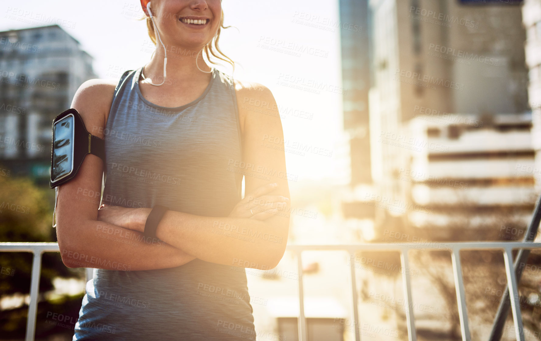 Buy stock photo Earphones, woman and runner in city with arms crossed for morning jog, exercise and outdoor workout. Athlete, training and girl with smile on bridge for running challenge, fitness or music playlist