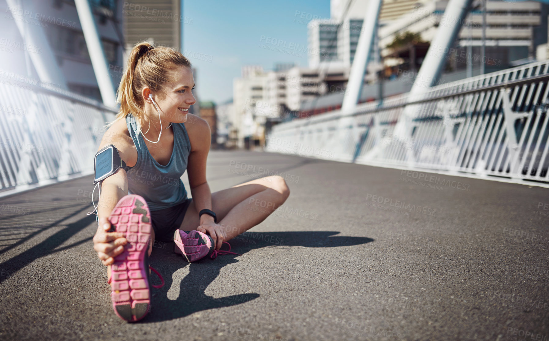 Buy stock photo Happy woman, fitness and stretching with earphones in city for exercise or workout preparation on bridge. Young, female person or runner with smile for body, leg or foot warm up in an urban town