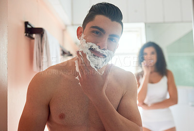 Buy stock photo Shot of a handsome young man shaving while his girlfriend brushes her teeth in the bathroom