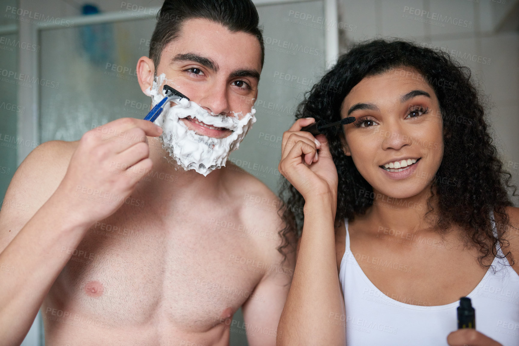 Buy stock photo Portrait of an attractive young woman applying mascara while her boyfriend shaves in the bathroom