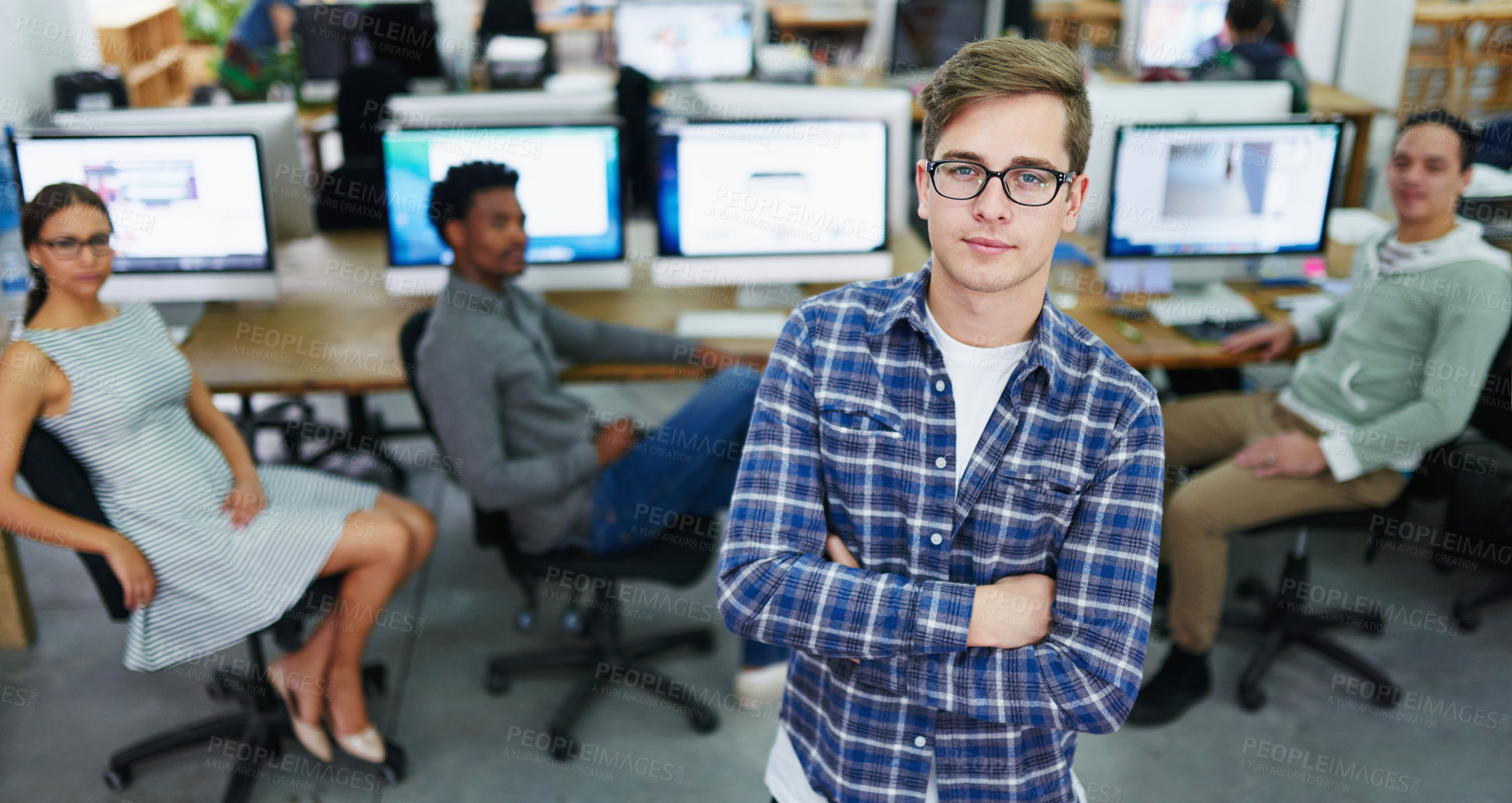 Buy stock photo Portrait of a focused young designer standing in an office with colleagues working in the background