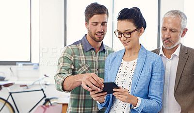 Buy stock photo Shot of a group of designers talking together over a digital tablet in an office