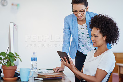 Buy stock photo Shot of two young designers talking together over a digital tablet in an office
