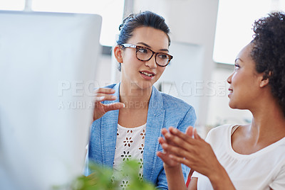 Buy stock photo Shot of two young designers talking together while sitting at a computer in an office