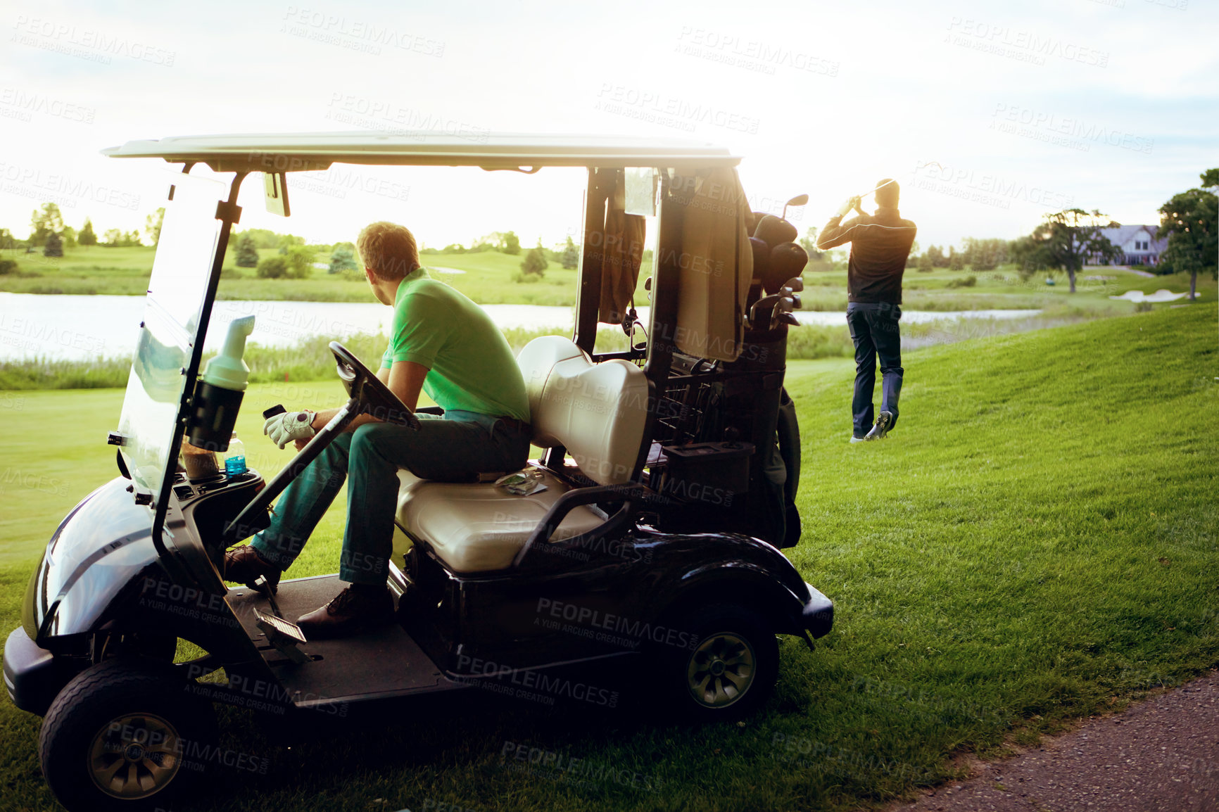 Buy stock photo Shot of a man watching his friend play golf while sitting in a golf cart