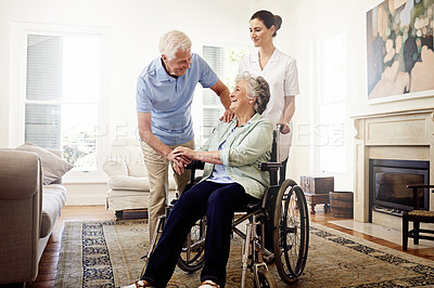 Buy stock photo Shot of a smiling caregiver with a senior woman in a wheelchair and her husband at home