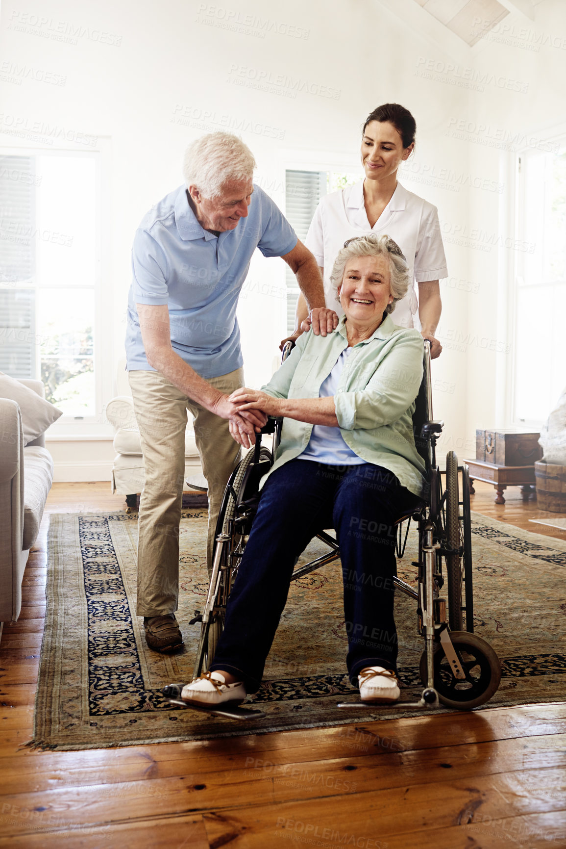 Buy stock photo Shot of a smiling caregiver with a senior woman in a wheelchair and her husband at home