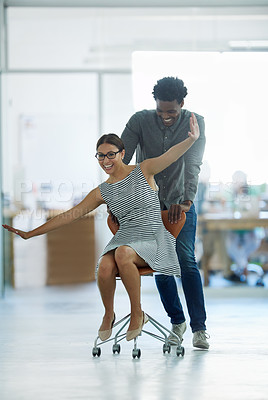 Buy stock photo Shot of a male coworker pushing his female coworker around an office in a chair