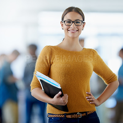 Buy stock photo Portrait of a young woman holding paperwork standing in an office with colleagues in the background