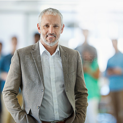 Buy stock photo Portrait of a smiling mature man standing in an office with colleagues in the background