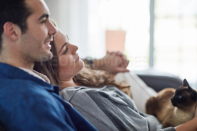 Buy stock photo Shot of a happy young couple relaxing on the sofa at home with their cat