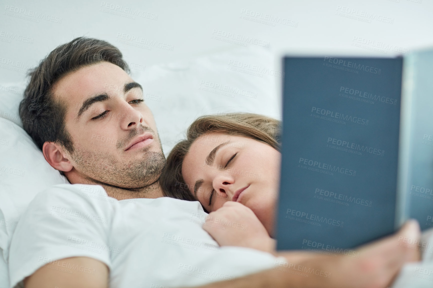 Buy stock photo Relax, love and couple in bed with book, comfort and peace, care and bonding in their home with safety. Calm, reading and male person with novel in bedroom with sleeping wife on weekend in a house