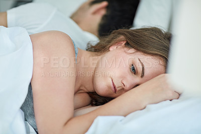Buy stock photo Shot of a young woman looking depressed while lying next to her husband in bed
