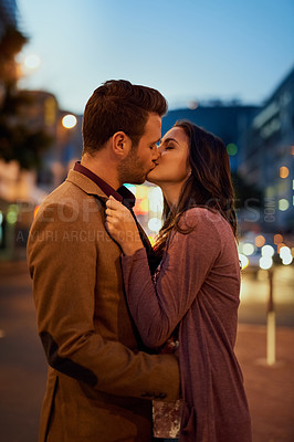 Buy stock photo Cropped shot of an affectionate young couple  sharing a kiss outside at night
