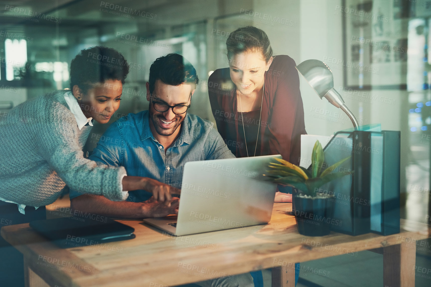 Buy stock photo Cropped shot of three young businesspeople looking at a laptop