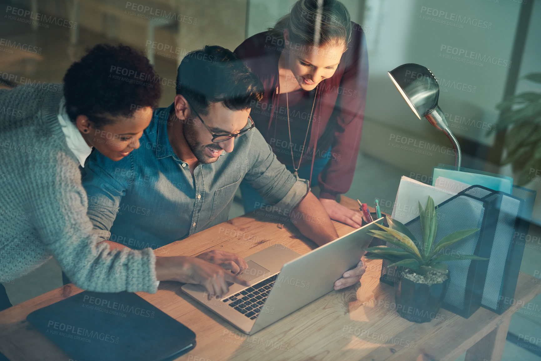 Buy stock photo High angle shot of three young businesspeople looking at a laptop